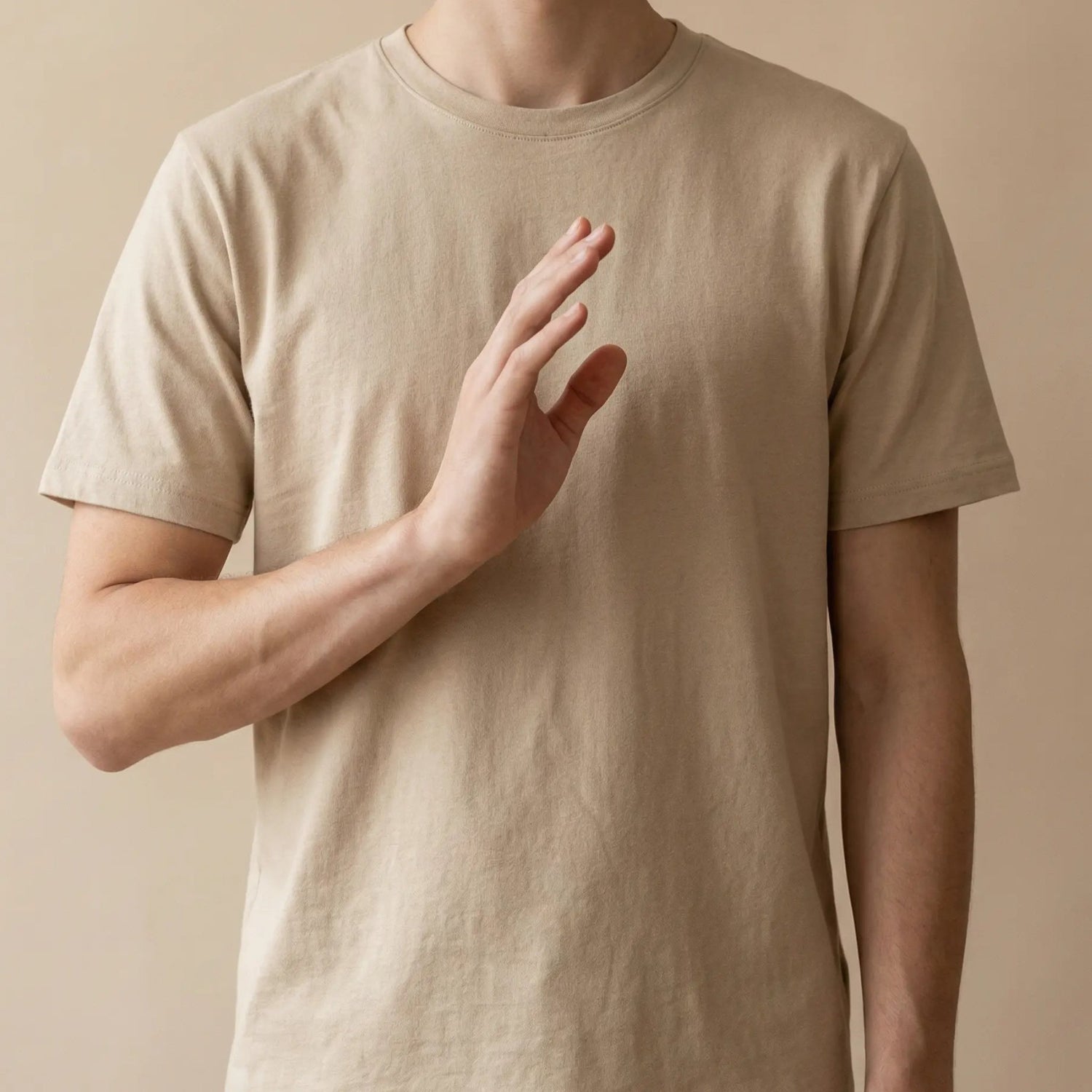 Person raising hand slightly while wearing neutral minimalist t-shirt